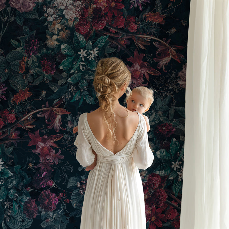 Woman in a white dress holding a baby against a floral wallpaper.