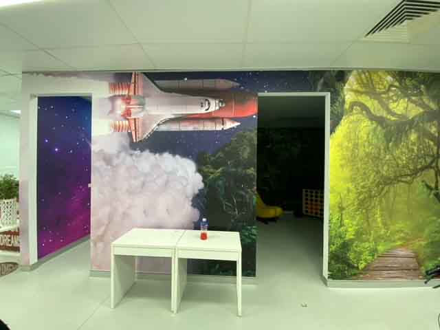 Room with colorful wall murals of a rocket and nature, featuring a small table.