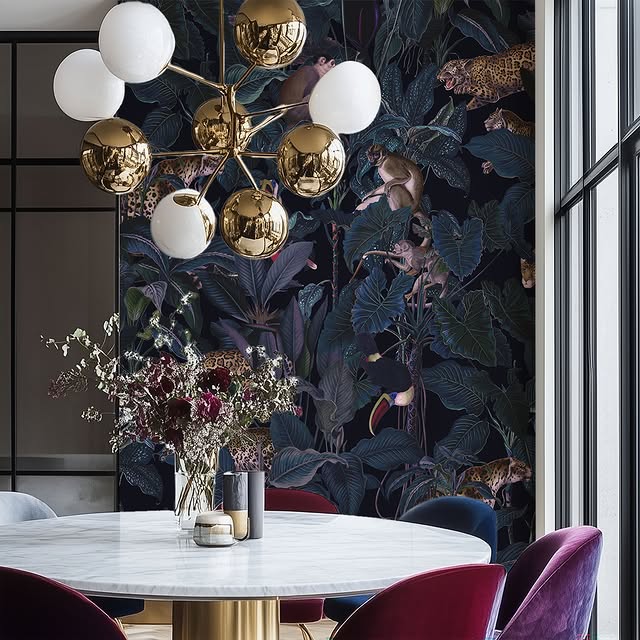 Modern chandelier above a round marble table with decorative elements in a stylish interior with a jungle wallpaper.