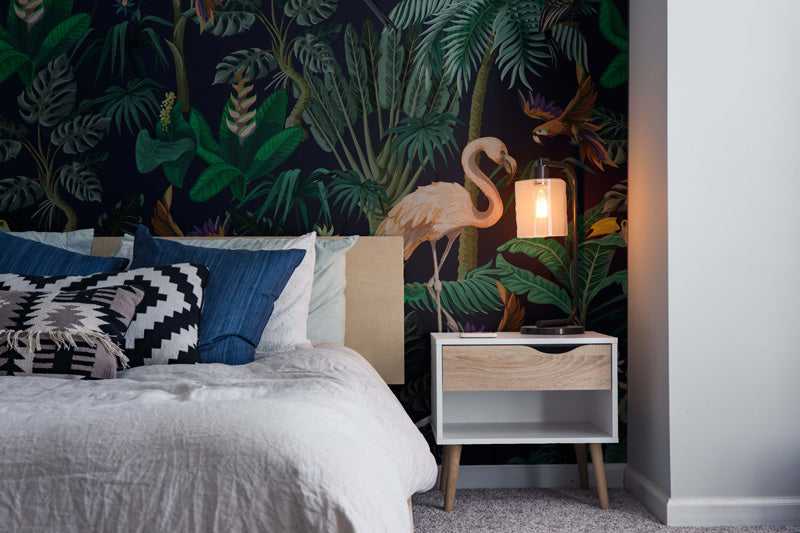 Bedroom with tropical wallpaper, bed with pillows, and nightstand with lamp.