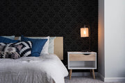 Modern bedroom with black wallpaper, bed with blue and patterned pillows, and nightstand with lamp.