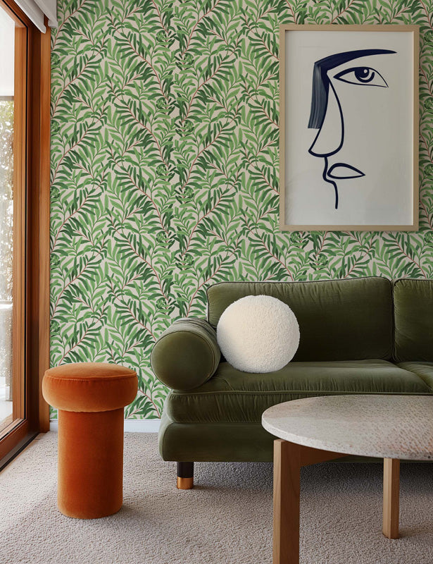 Living room with green sofa, orange stool, and abstract art on leafy wallpaper.