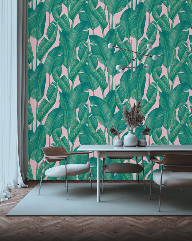 Dining room with a pink wall featuring a green leaf wallpaper design and a table with chairs.