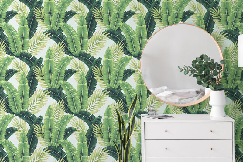 White dresser with round mirror against a tropical leaf wallpaper.