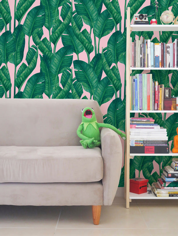 Living room with a green frog plush toy on a beige sofa against a pink wallpaper with green leaf design.