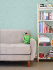Green plush toy on a beige sofa against a blue wallpaper with a bookshelf.