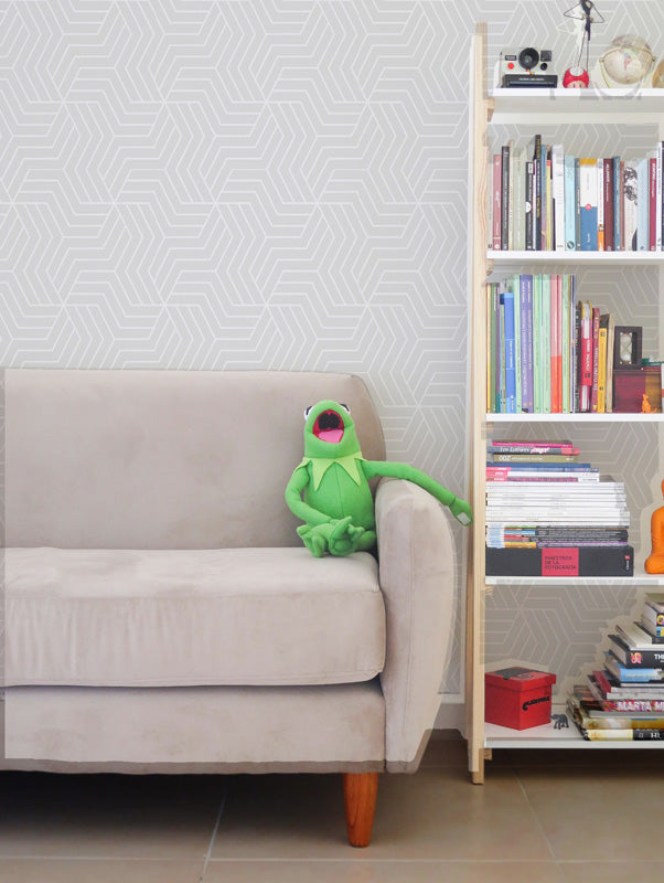 Green plush toy on a beige sofa next to a bookshelf with books against a white wallpaper.