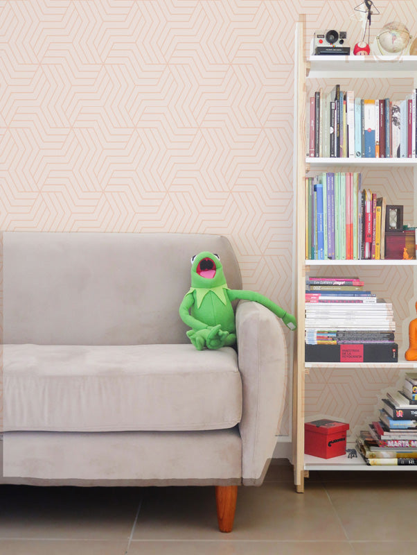 Green plush toy on a beige sofa next to a bookshelf with books and pink wallpaper.