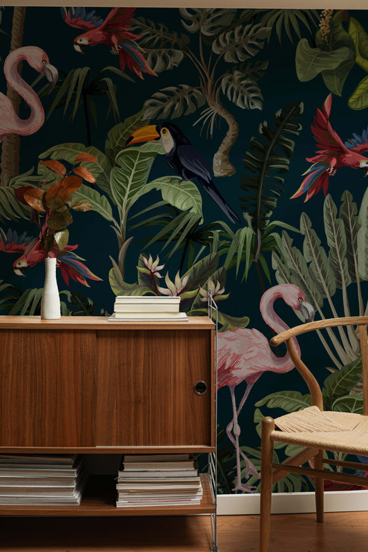 Room interior with wooden cabinet and chair against a tropical wallpaper with flamingos and parrots.