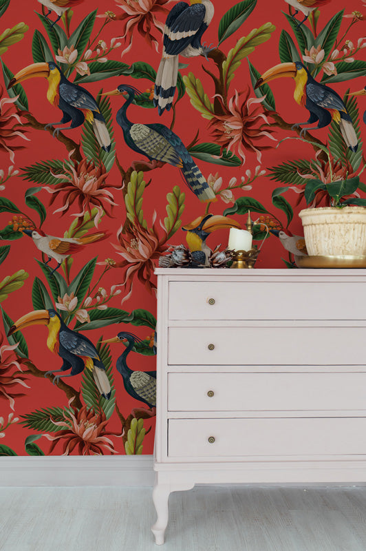 White dresser against a vibrant red wallpaper with tropical bird and flower pattern