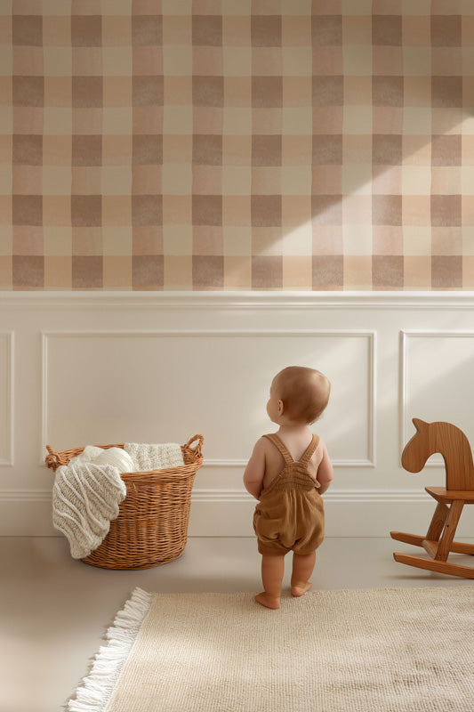 Baby in a brown romper standing in a room with checkered wallpaper and wooden toys.