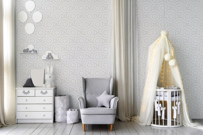 Nursery room with gray armchair, crib, and decorative elements against a geometric wallpaper.