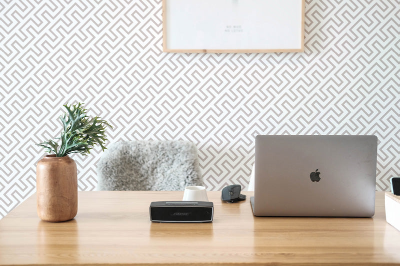 Laptop on a wooden desk with decorative wallpaper.