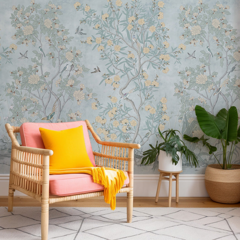 Wicker chair with pink cushion and yellow blanket against a floral wallpaper.