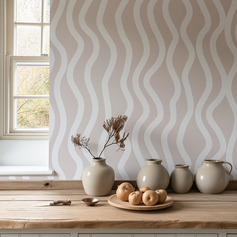 Decorative vases and a plate with apples on a wooden surface against a wavy wallpaper.