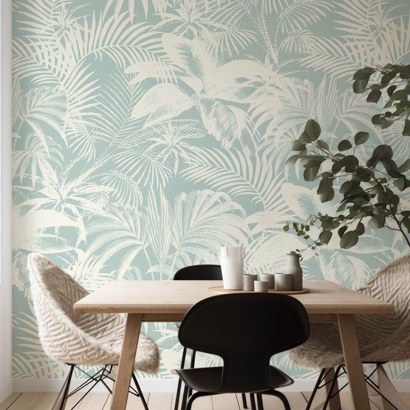 Dining area with a table and chairs against a wall with tropical leaf wallpaper.